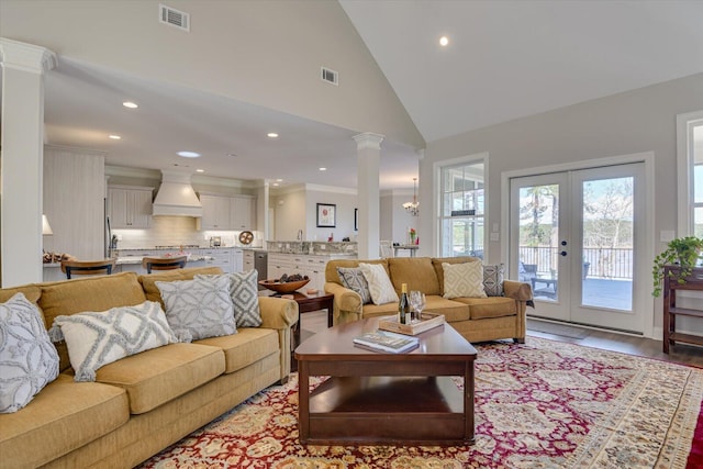 living area with high vaulted ceiling, light wood-type flooring, visible vents, and decorative columns