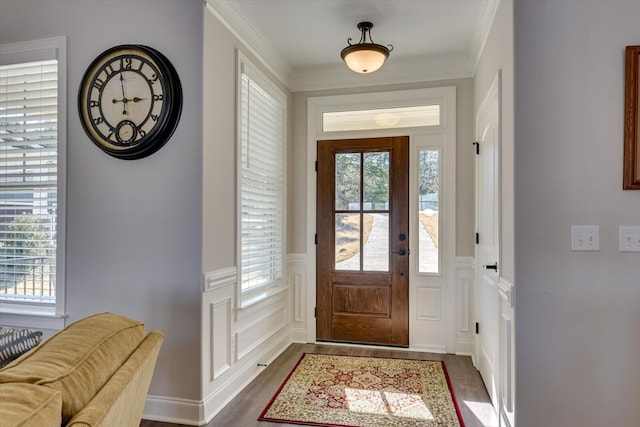 foyer entrance with ornamental molding, dark wood-type flooring, wainscoting, and a decorative wall