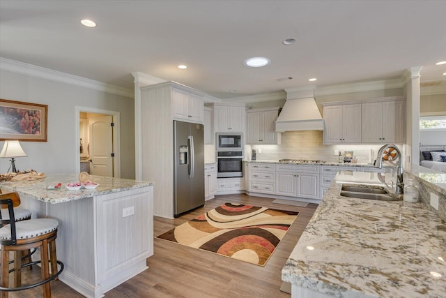 kitchen with white cabinets, light stone counters, stainless steel appliances, premium range hood, and a sink