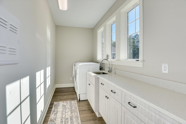 laundry area featuring cabinet space, baseboards, dark wood-style flooring, washing machine and clothes dryer, and a sink