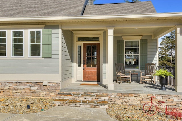 entrance to property featuring covered porch and a shingled roof