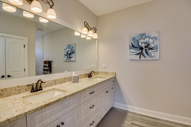 full bathroom featuring double vanity, baseboards, a sink, and wood finished floors