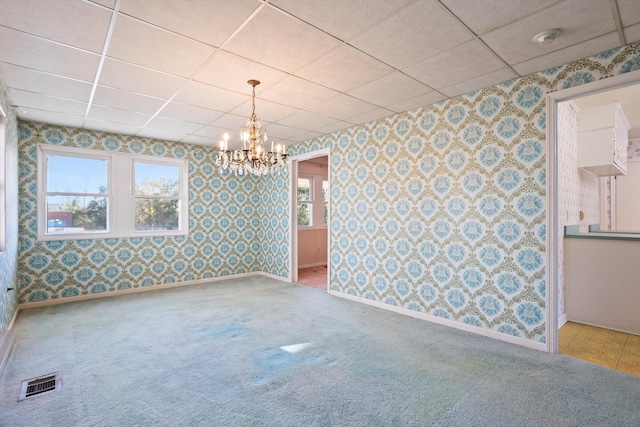 carpeted empty room featuring a paneled ceiling and a notable chandelier