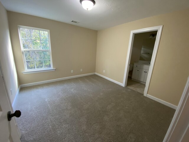 unfurnished bedroom featuring light colored carpet and ensuite bath