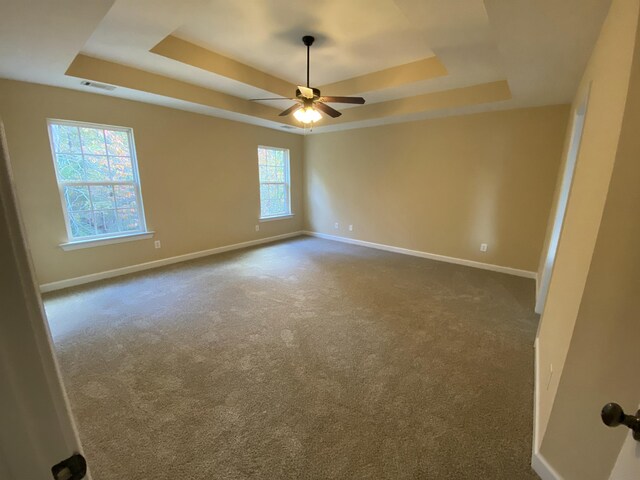 carpeted spare room with ceiling fan and a raised ceiling