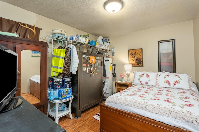 bedroom with water heater, light hardwood / wood-style floors, and a textured ceiling