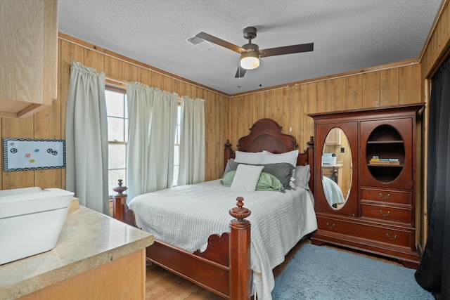 bedroom featuring a textured ceiling, light hardwood / wood-style floors, ceiling fan, and wooden walls