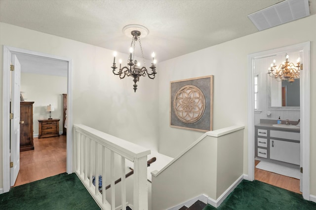 corridor featuring a textured ceiling, an inviting chandelier, dark wood-type flooring, and sink