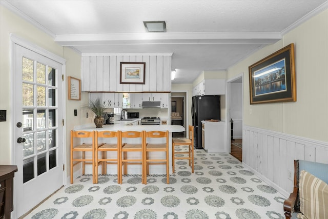 kitchen with kitchen peninsula, a kitchen bar, black fridge, stainless steel range oven, and white cabinets