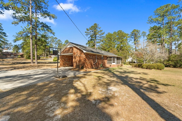 view of side of property featuring brick siding, a lawn, and a sunroom