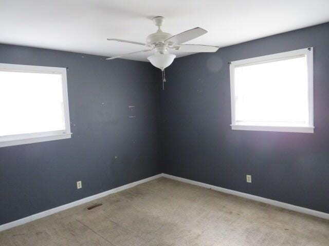 empty room featuring ceiling fan, plenty of natural light, and light carpet