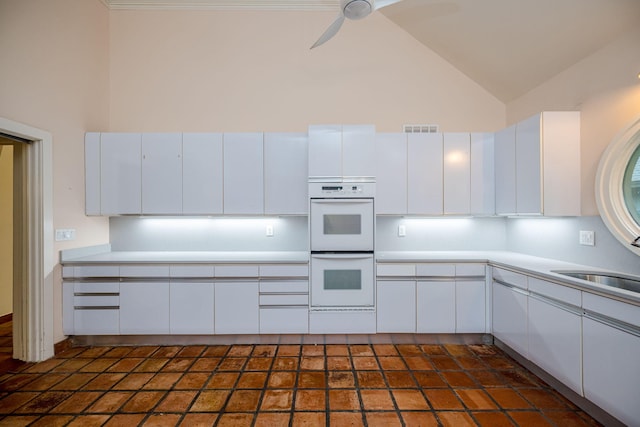 kitchen with high vaulted ceiling, white cabinets, sink, ceiling fan, and double oven