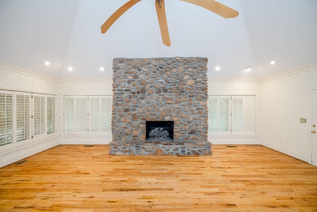 unfurnished living room with wood walls, ceiling fan, light hardwood / wood-style floors, and a stone fireplace