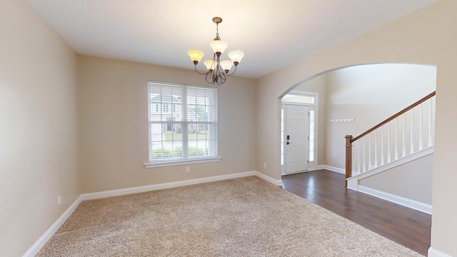 foyer entrance with baseboards, arched walkways, stairway, dark wood-style flooring, and an inviting chandelier