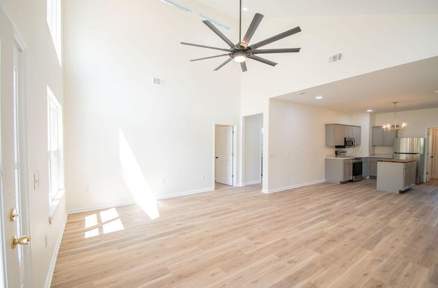 unfurnished living room with ceiling fan with notable chandelier, light hardwood / wood-style floors, and a high ceiling