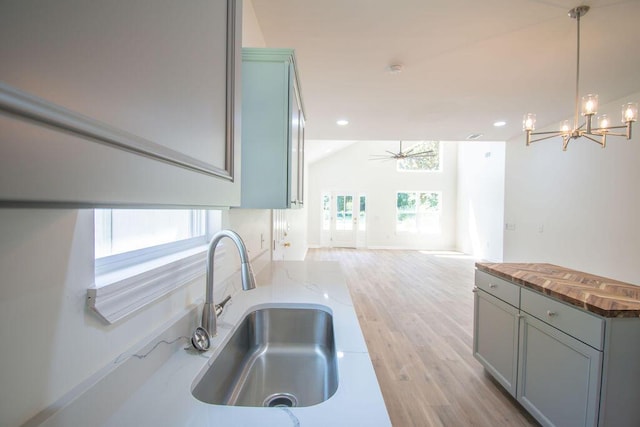 kitchen featuring ceiling fan with notable chandelier, sink, pendant lighting, light hardwood / wood-style flooring, and butcher block counters