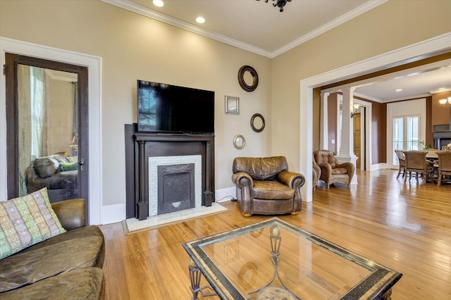 living room featuring wood-type flooring, decorative columns, crown molding, and a brick fireplace