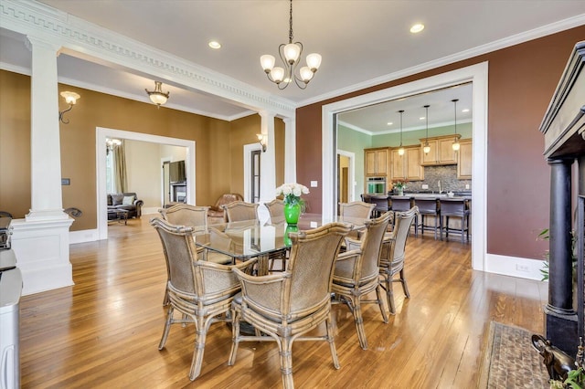 dining space featuring a chandelier, light wood-type flooring, decorative columns, and crown molding