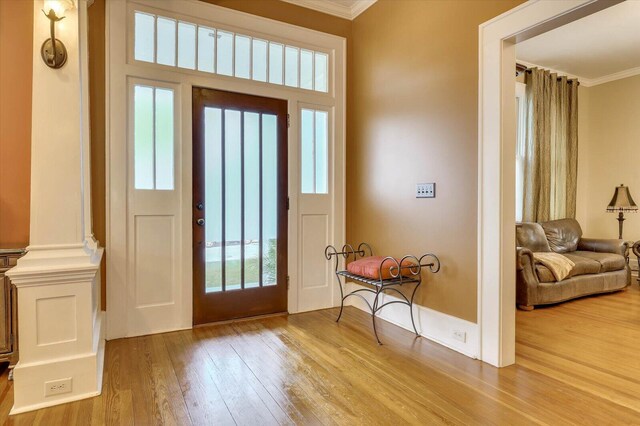 entrance foyer with plenty of natural light, ornate columns, ornamental molding, and light hardwood / wood-style flooring