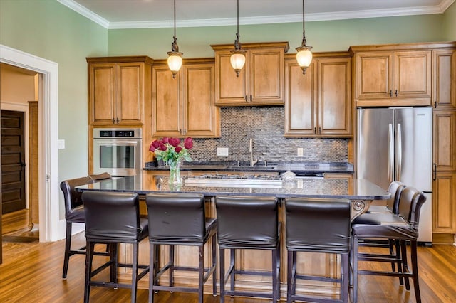 kitchen featuring tasteful backsplash, ornamental molding, stainless steel appliances, a kitchen island with sink, and dark stone countertops