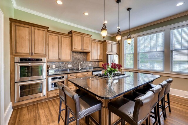 kitchen with a center island, sink, dark stone counters, decorative light fixtures, and appliances with stainless steel finishes