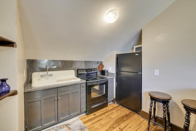 kitchen featuring black appliances, light wood-type flooring, sink, and vaulted ceiling