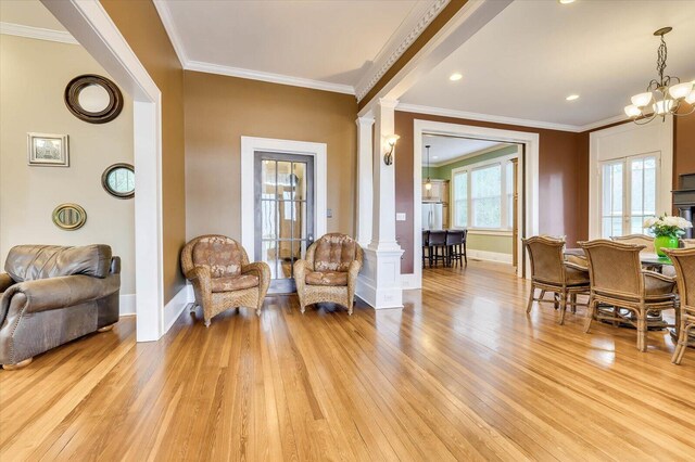 living area featuring decorative columns, crown molding, light wood-type flooring, and an inviting chandelier