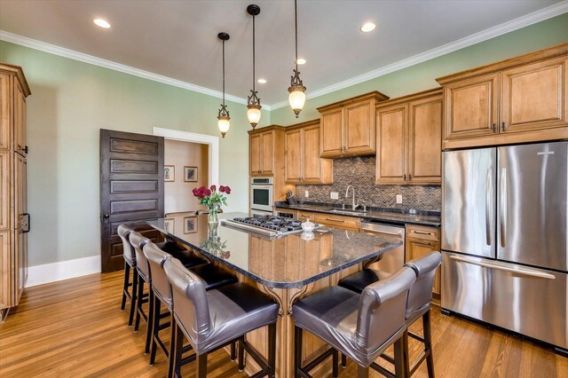 kitchen with a center island, pendant lighting, dark stone counters, appliances with stainless steel finishes, and ornamental molding