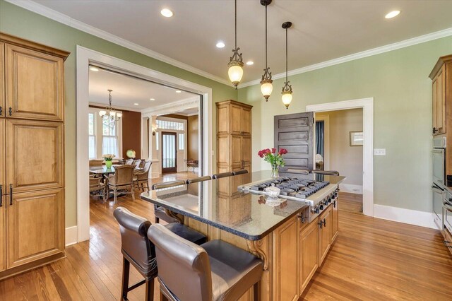 kitchen with dark stone counters, crown molding, a kitchen island, a kitchen bar, and stainless steel gas cooktop