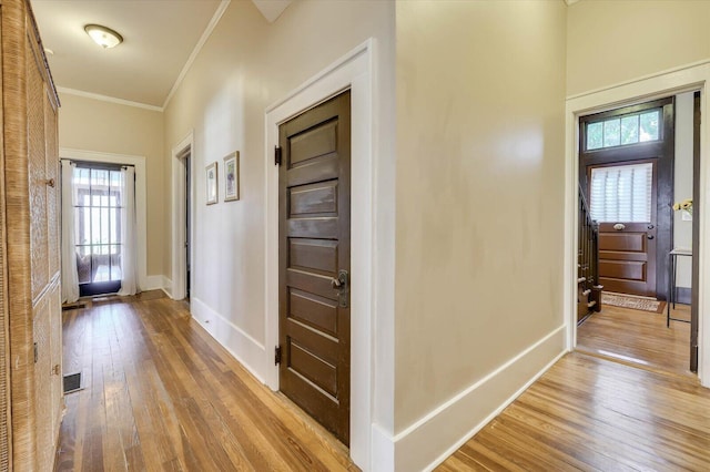 hallway with a healthy amount of sunlight, light hardwood / wood-style floors, and crown molding