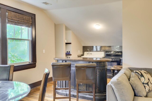 kitchen featuring lofted ceiling, sink, electric range, stainless steel counters, and light hardwood / wood-style floors