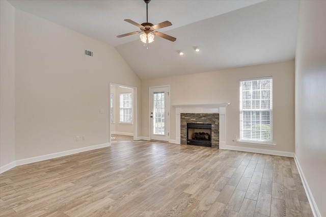 unfurnished living room featuring ceiling fan, light hardwood / wood-style flooring, a wealth of natural light, and a stone fireplace