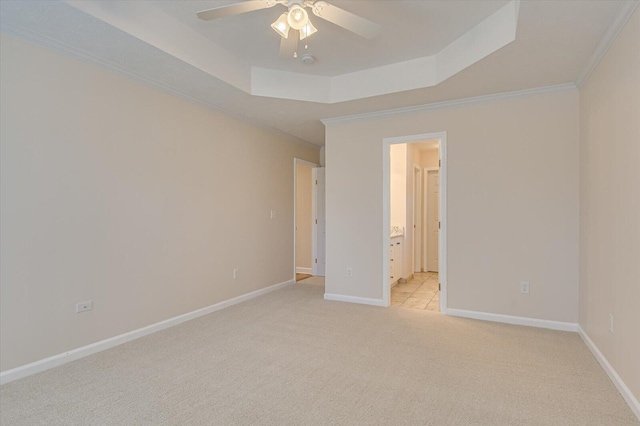 unfurnished bedroom featuring a raised ceiling, light colored carpet, crown molding, ceiling fan, and ensuite bathroom