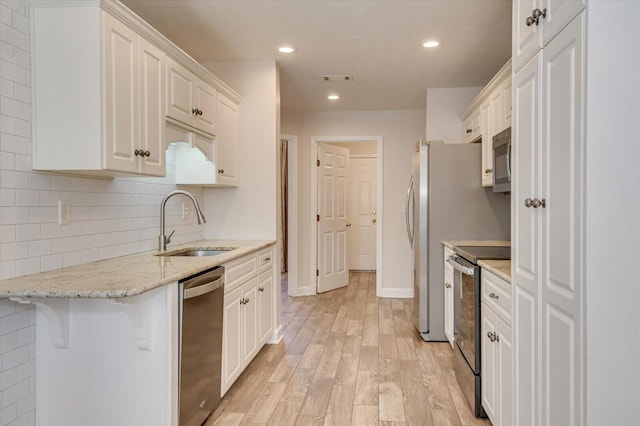 kitchen featuring appliances with stainless steel finishes, light wood-type flooring, light stone counters, white cabinets, and sink