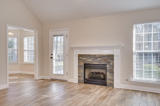 unfurnished living room featuring light hardwood / wood-style flooring, a stone fireplace, vaulted ceiling, and a wealth of natural light