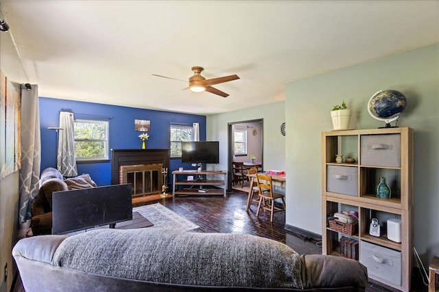 living area with a fireplace, wood-type flooring, baseboards, and ceiling fan
