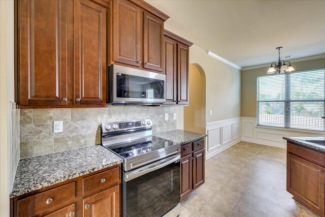 kitchen with dark stone countertops, crown molding, a chandelier, and appliances with stainless steel finishes