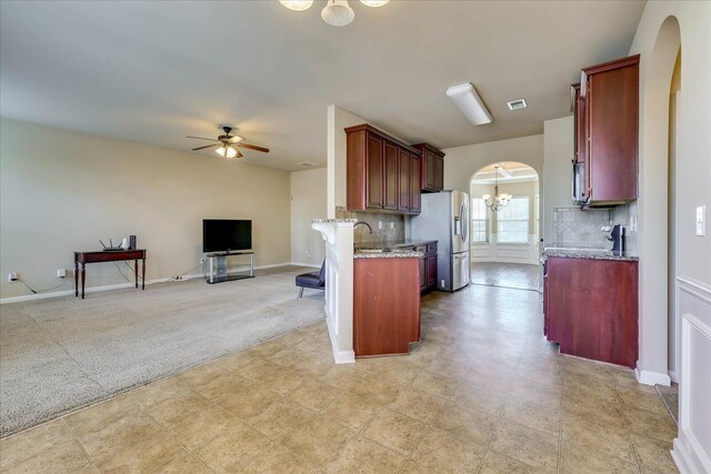 kitchen featuring ceiling fan with notable chandelier, kitchen peninsula, tasteful backsplash, light colored carpet, and stainless steel fridge with ice dispenser