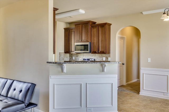 kitchen featuring a kitchen bar, kitchen peninsula, light stone countertops, and tasteful backsplash