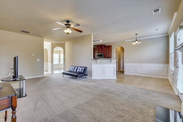 living room featuring ceiling fan with notable chandelier, crown molding, and light carpet