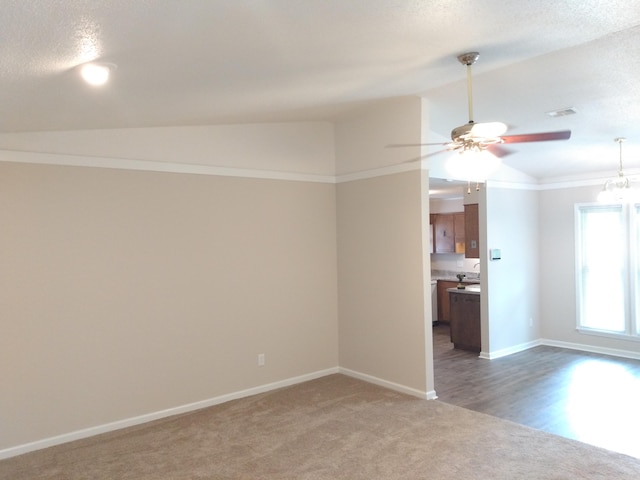 carpeted empty room with a textured ceiling, ceiling fan with notable chandelier, and vaulted ceiling