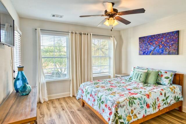 bedroom with a ceiling fan, wood finished floors, visible vents, and baseboards