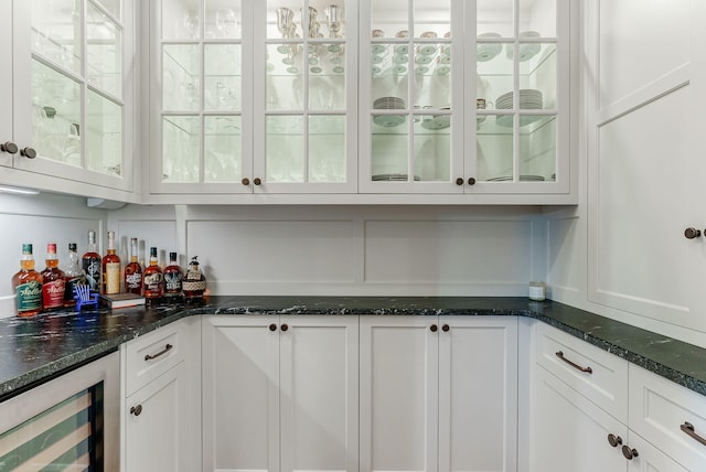 bar with white cabinetry, beverage cooler, and dark stone countertops