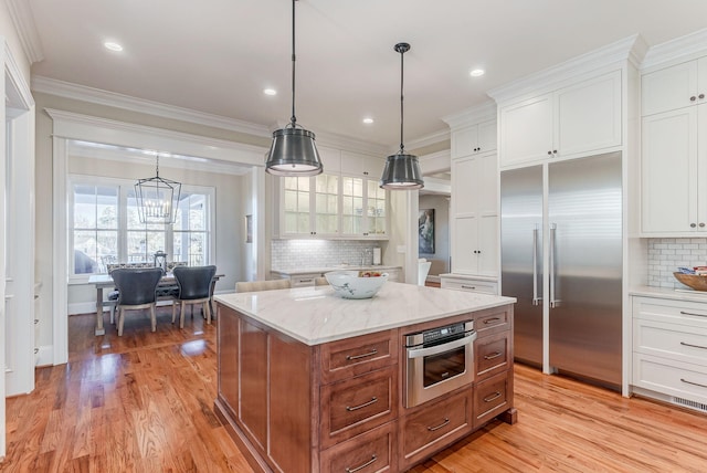 kitchen with white cabinetry, a center island, hanging light fixtures, stainless steel appliances, and light stone counters