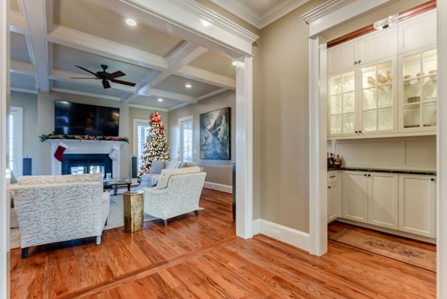 living room with beam ceiling, ceiling fan, coffered ceiling, light hardwood / wood-style flooring, and crown molding