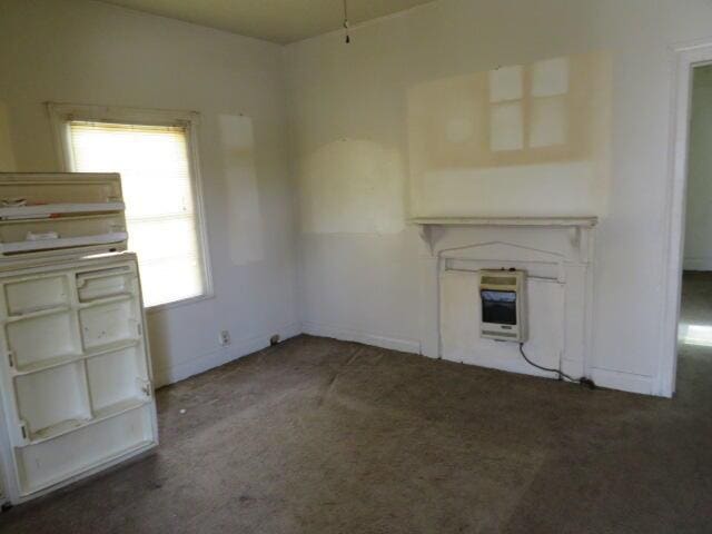 unfurnished living room featuring baseboards, dark carpet, and heating unit