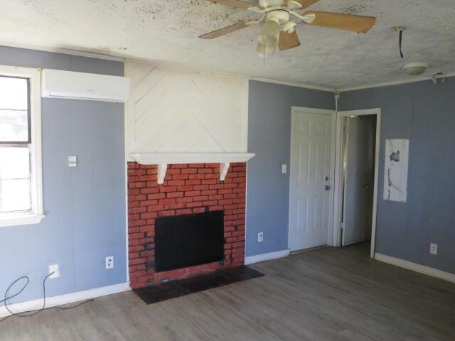 unfurnished living room featuring baseboards, a wall unit AC, wood finished floors, a textured ceiling, and a brick fireplace