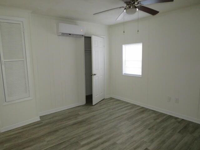 unfurnished bedroom featuring a wall mounted AC, wood finished floors, and baseboards