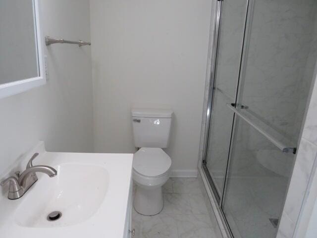 bathroom featuring marble finish floor, toilet, a stall shower, vanity, and baseboards