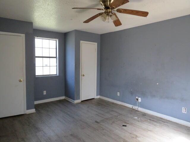 unfurnished bedroom featuring ceiling fan, a textured ceiling, baseboards, and wood finished floors